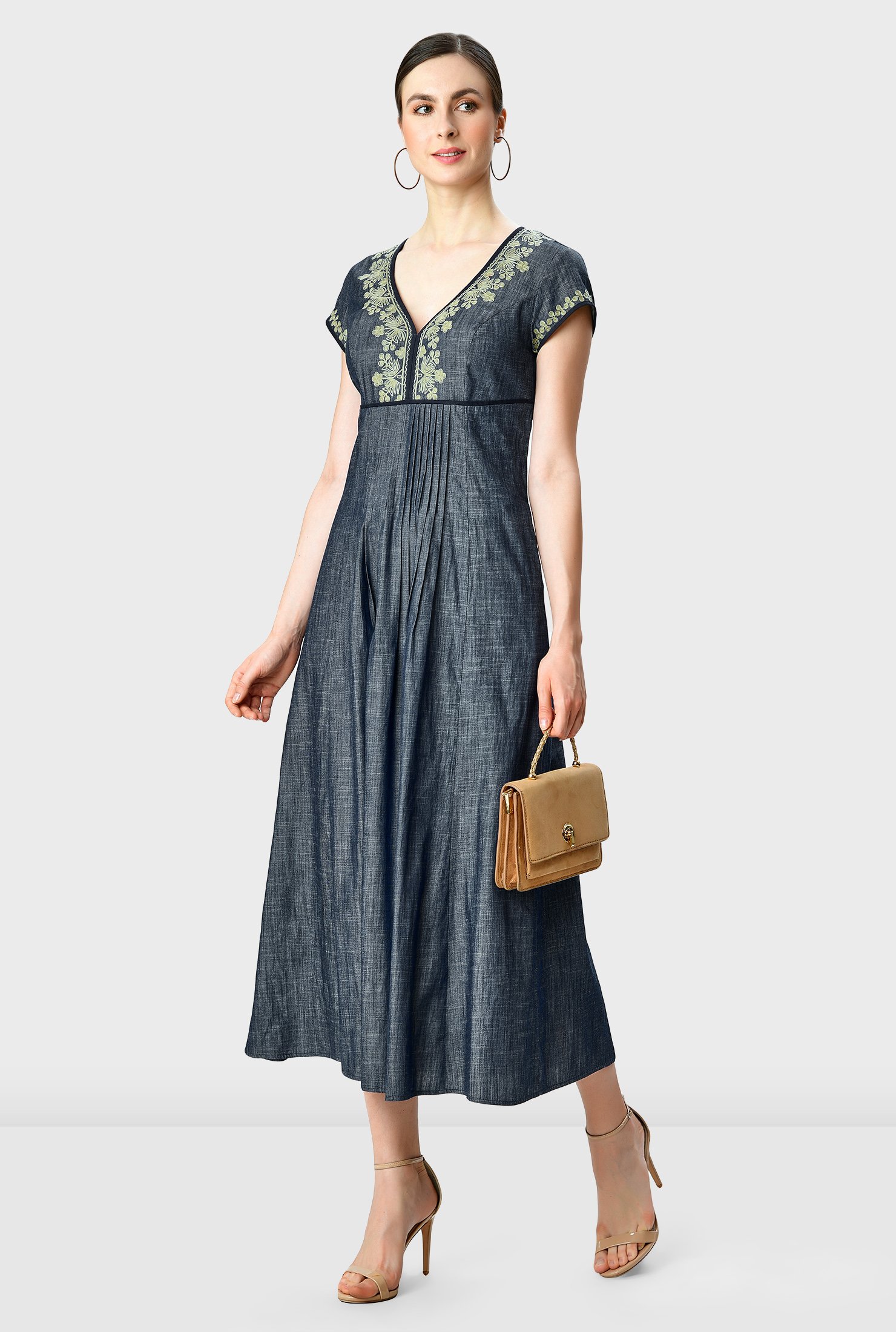 Artful embroidery blooms on our light cotton chambray dress fashioned with front and back pintuck pleats that release from the contrast empire waist to the full flare skirt. 